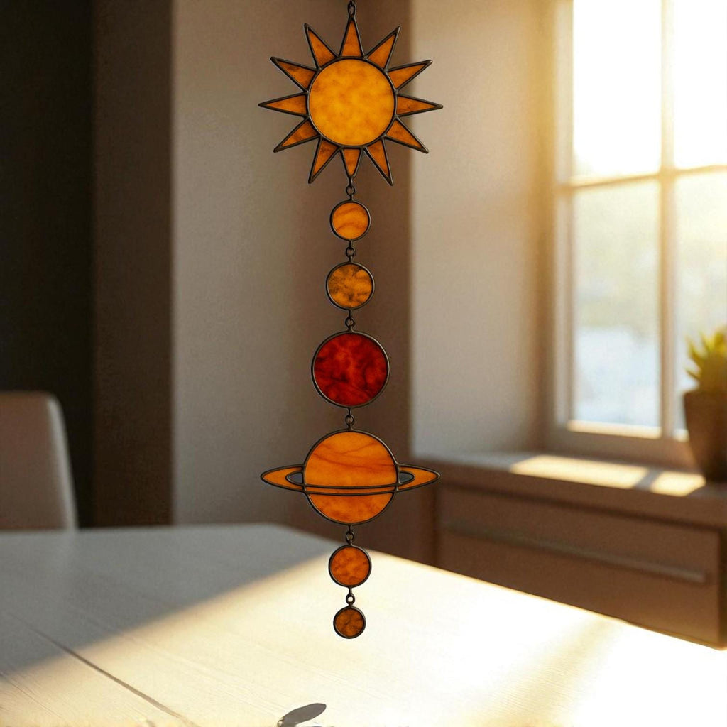 Three handcrafted stained glass suncatchers depicting the solar system and planets, featuring semi-circle, sun, and large sun designs – with vibrant colors like yellow, red, blue, orange, and green – hanging by metal chains in front of a sunlit window.