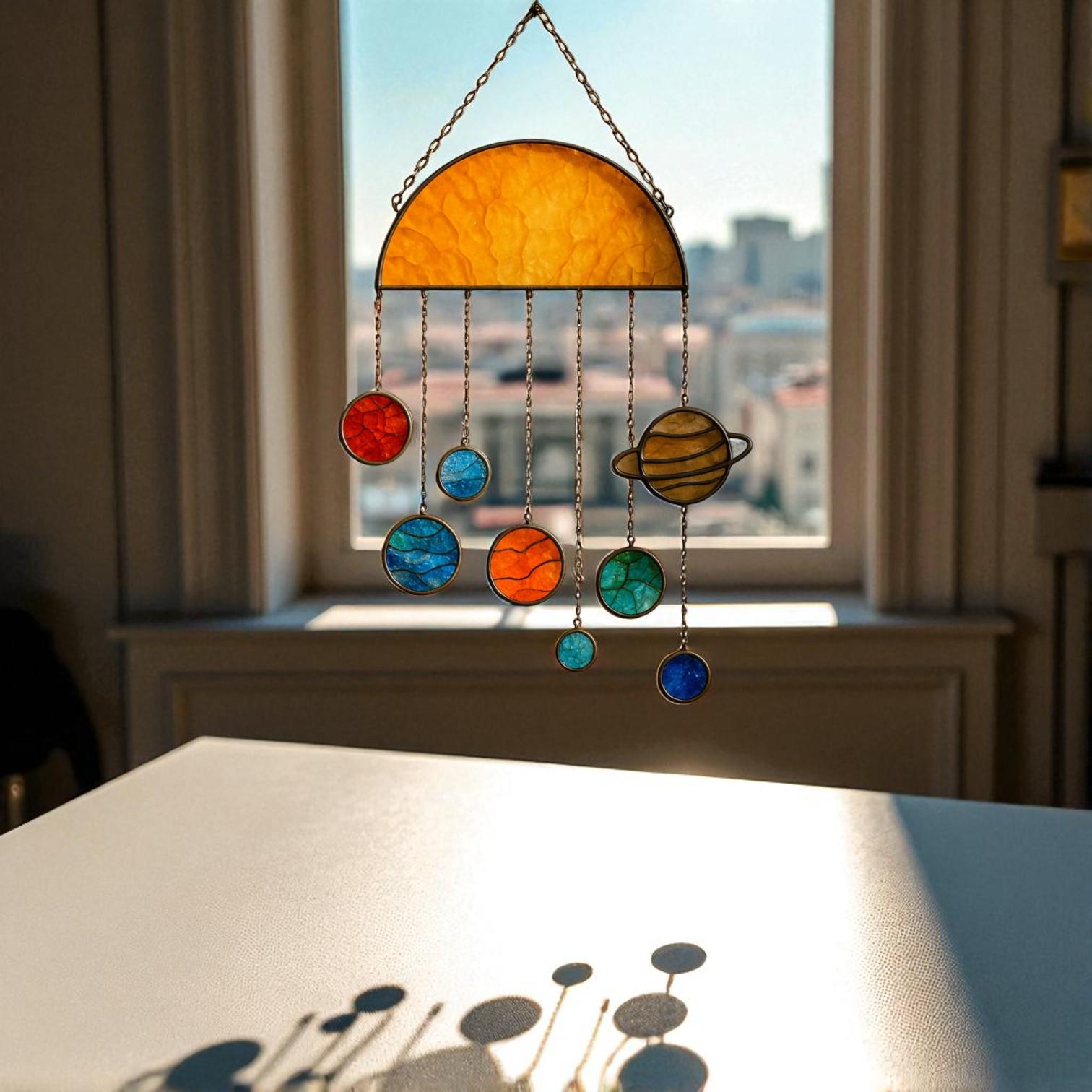 Three handcrafted stained glass suncatchers depicting the solar system and planets, featuring semi-circle, sun, and large sun designs – with vibrant colors like yellow, red, blue, orange, and green – hanging by metal chains in front of a sunlit window.