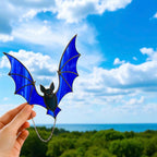 Close-up of a person holding stained glass bat suncatcher against the sky. The blue wings sparkle in natural sunlight, showcasing whimsical handmade Halloween decor