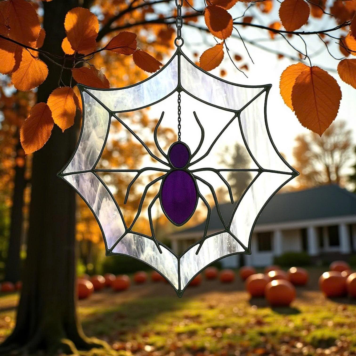 Stained glass spider web suncatcher with purple spider hanging from autumn tree branches, pumpkins and fall colors in the background, Halloween window hanging