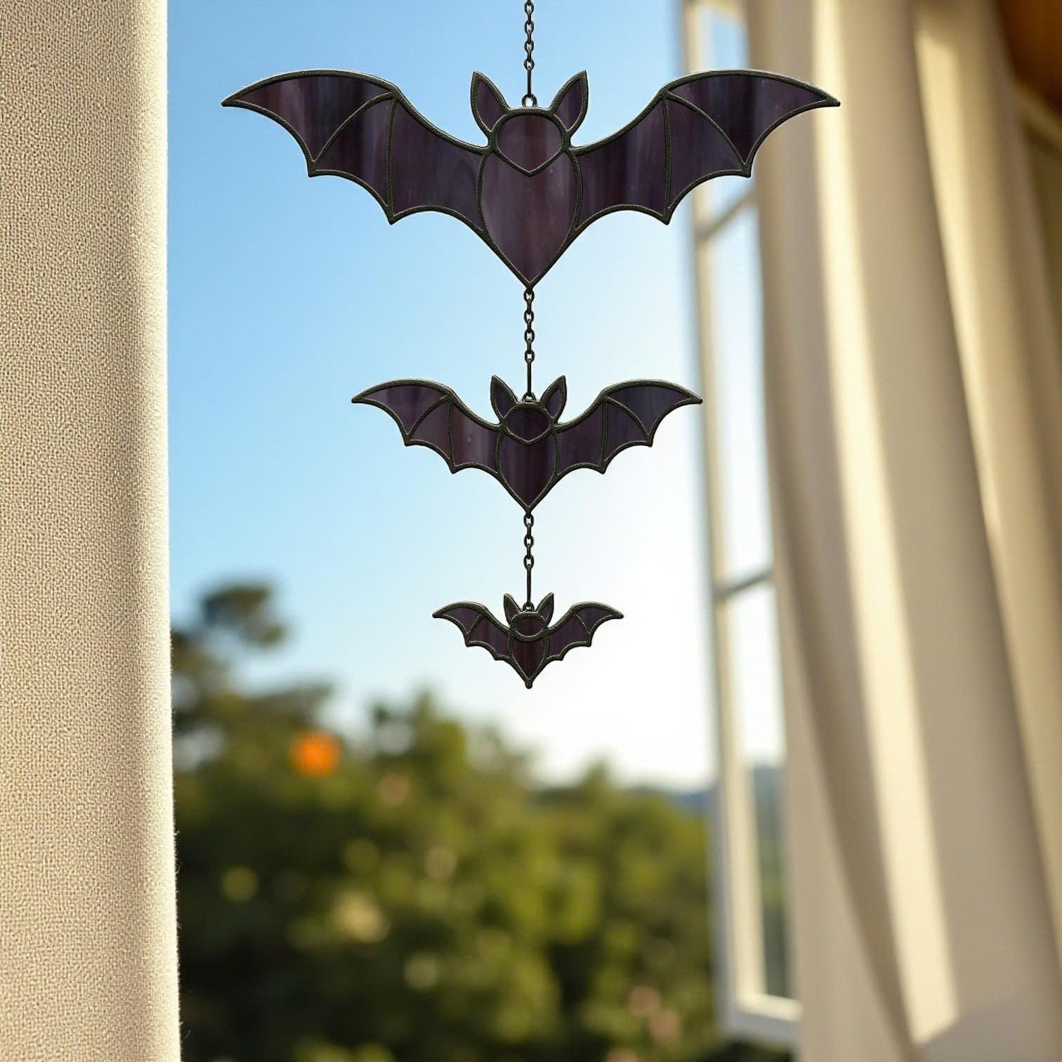 Handcrafted stained glass bat suncatcher hanging indoors by the window, whimsical Halloween gothic style.