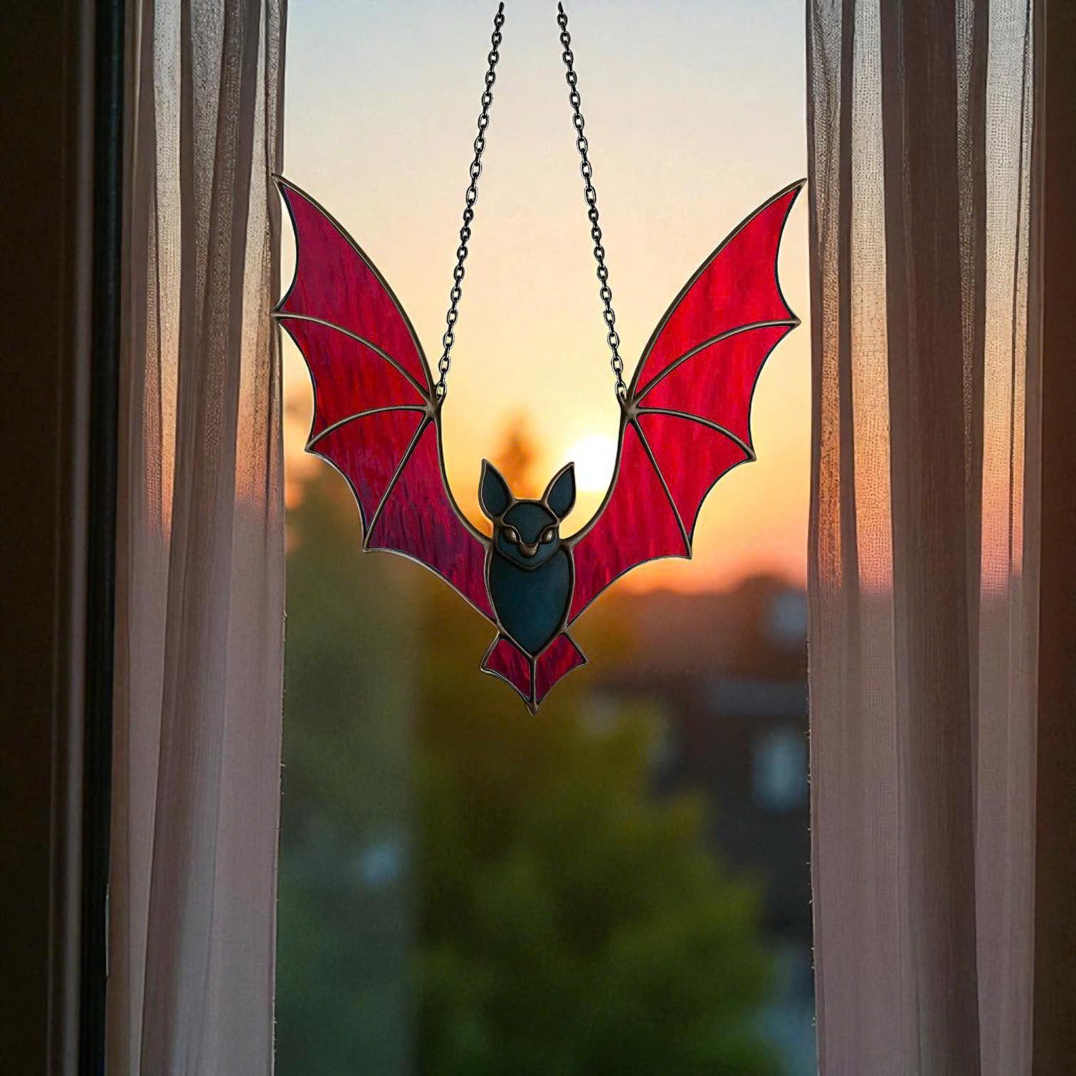 Red stained glass bat suncatcher hanging on a window with sunset background. Striking Halloween gothic decor and symbolic handmade glass art