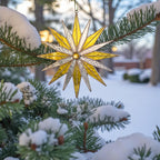 Detailed view of a stained glass snowflake ornament with yellow and silver colors, hanging delicately on a snow-covered Christmas tree.