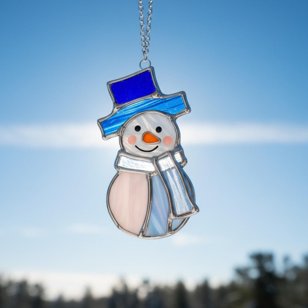 Stained glass snowman (Style #3) hanging on a snow-covered pine branch in a winter forest.