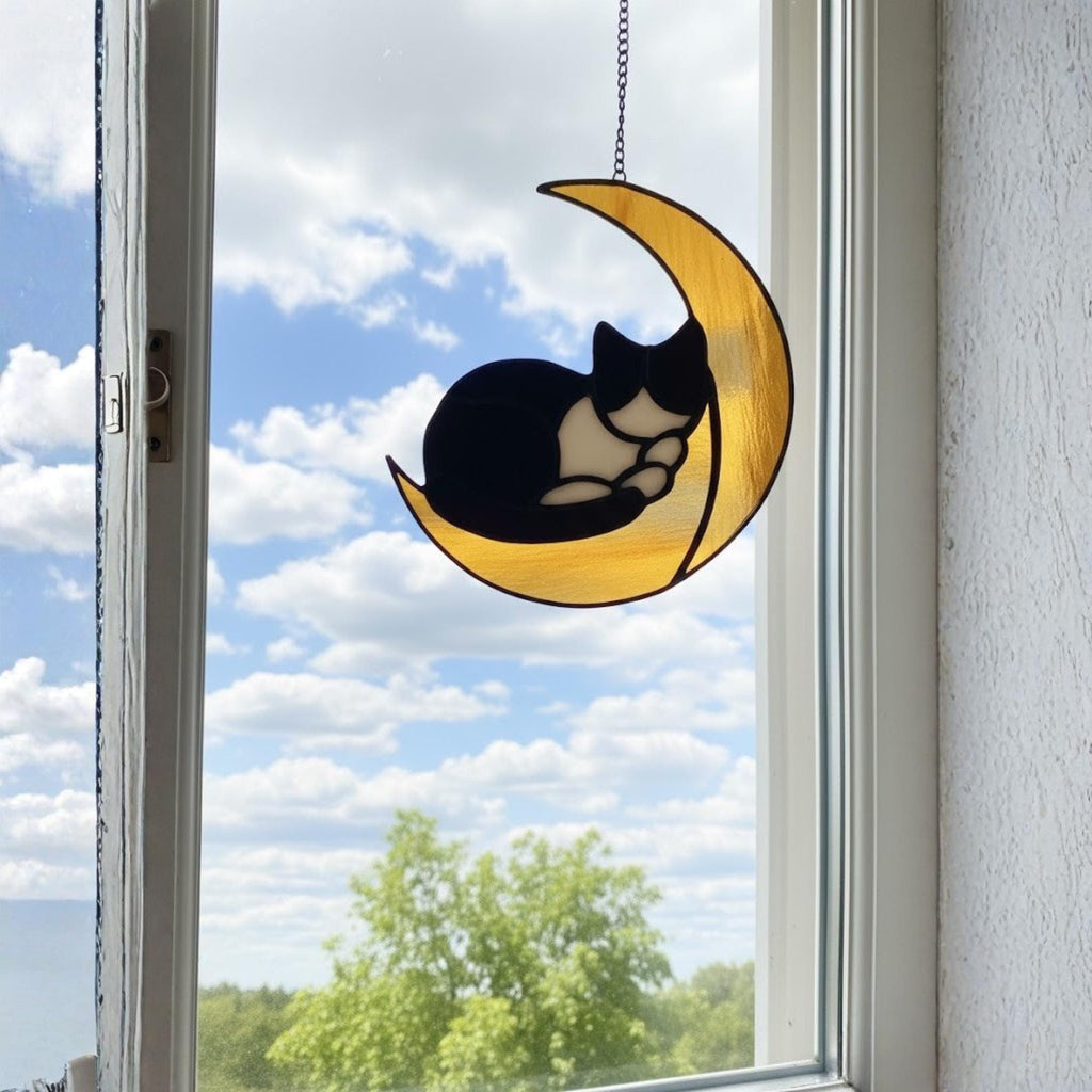Stained glass cat moon suncatcher hanging above white bed, minimal bedroom wall decor