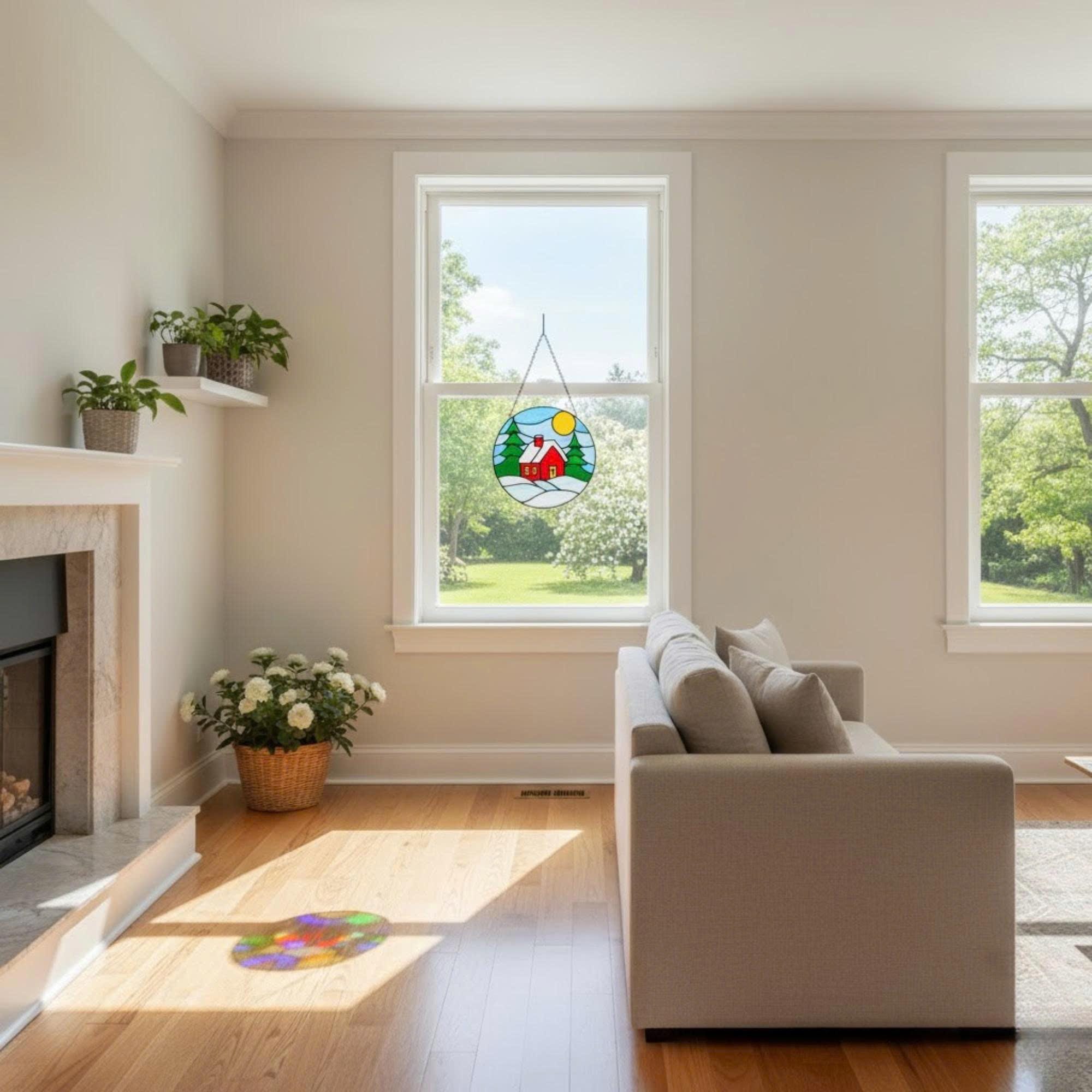 Sunlit bedroom with stained glass winter house art hanging on window, cozy handmade decor.