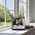 Woman hanging winter cottage stained glass decor on bright window, colorful handmade glass reflections.