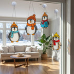 Set of handmade stained glass penguin suncatchers hanging on window, cute winter holiday home decor glowing in sunlight.