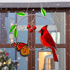 Stained glass cardinal hanging on a window with soft, glowing holiday lights in the background.
