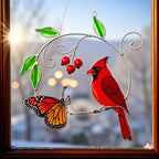 Stained glass ornament featuring a red cardinal perched on a branch with a butterfly and cherries, hanging by a window.
