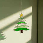 Stained glass tree suncatcher (Style #3) hanging in a window, with a church and cross visible in the background.