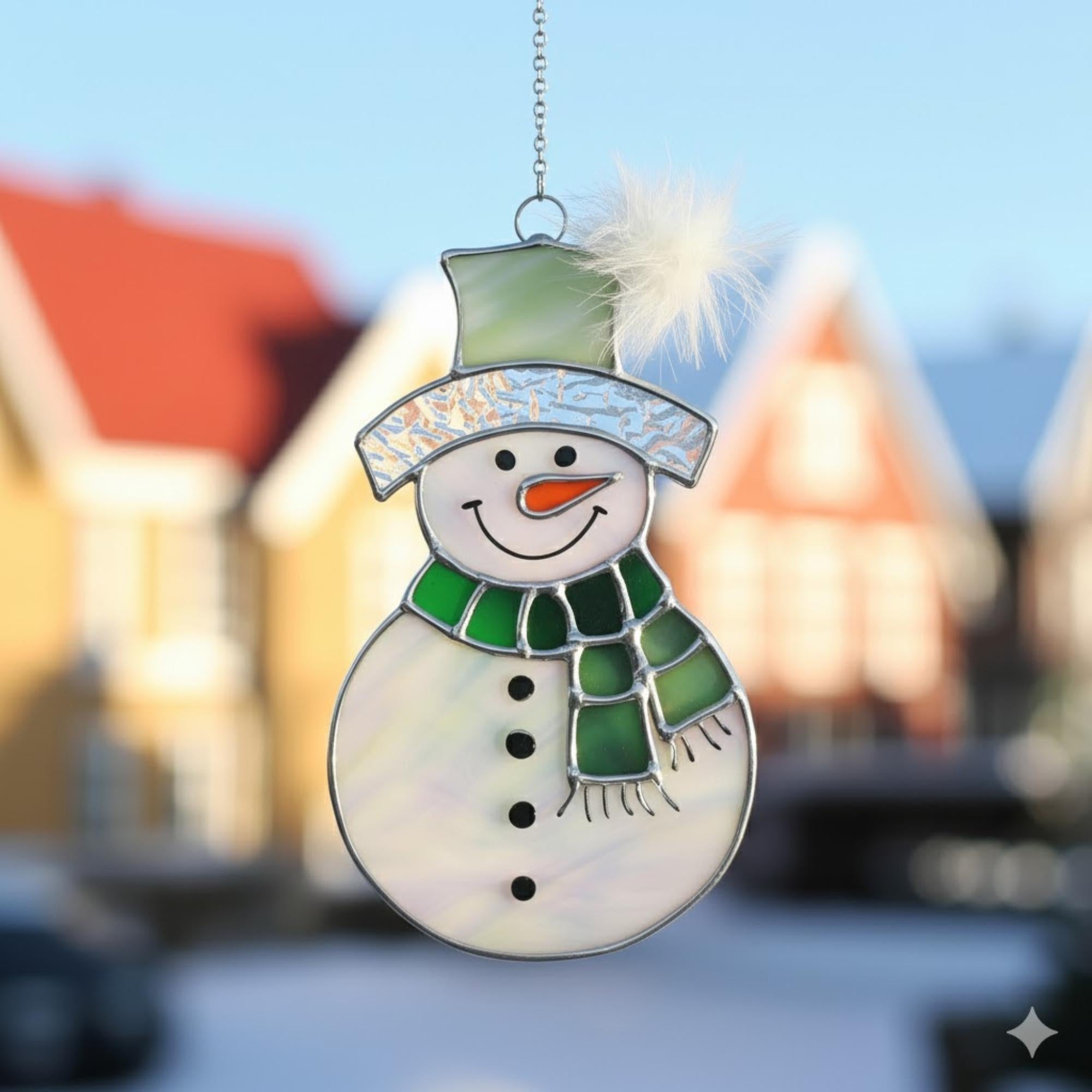 Stained glass snowman (Style #3, red hat, blue scarf) hanging in a window overlooking a blurred outdoor tree scene.