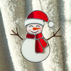 Stained glass snowman (Style #5) hanging in a window with a clear, bright view of the winter scene outside.