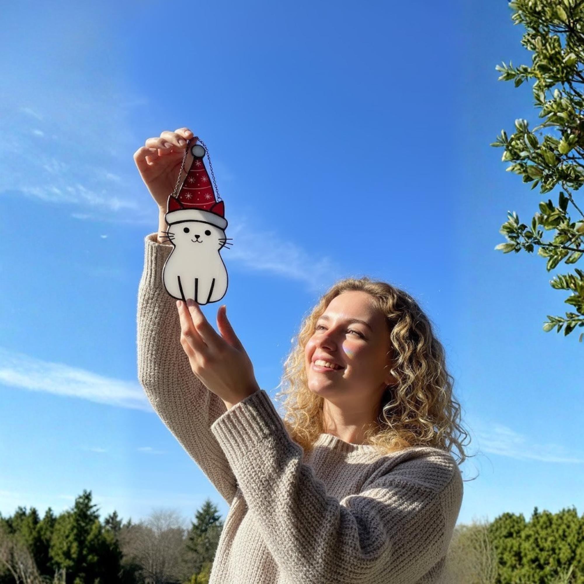 Smiling woman holding cat glass ornament in sunlight – cheerful handmade Christmas decoration.