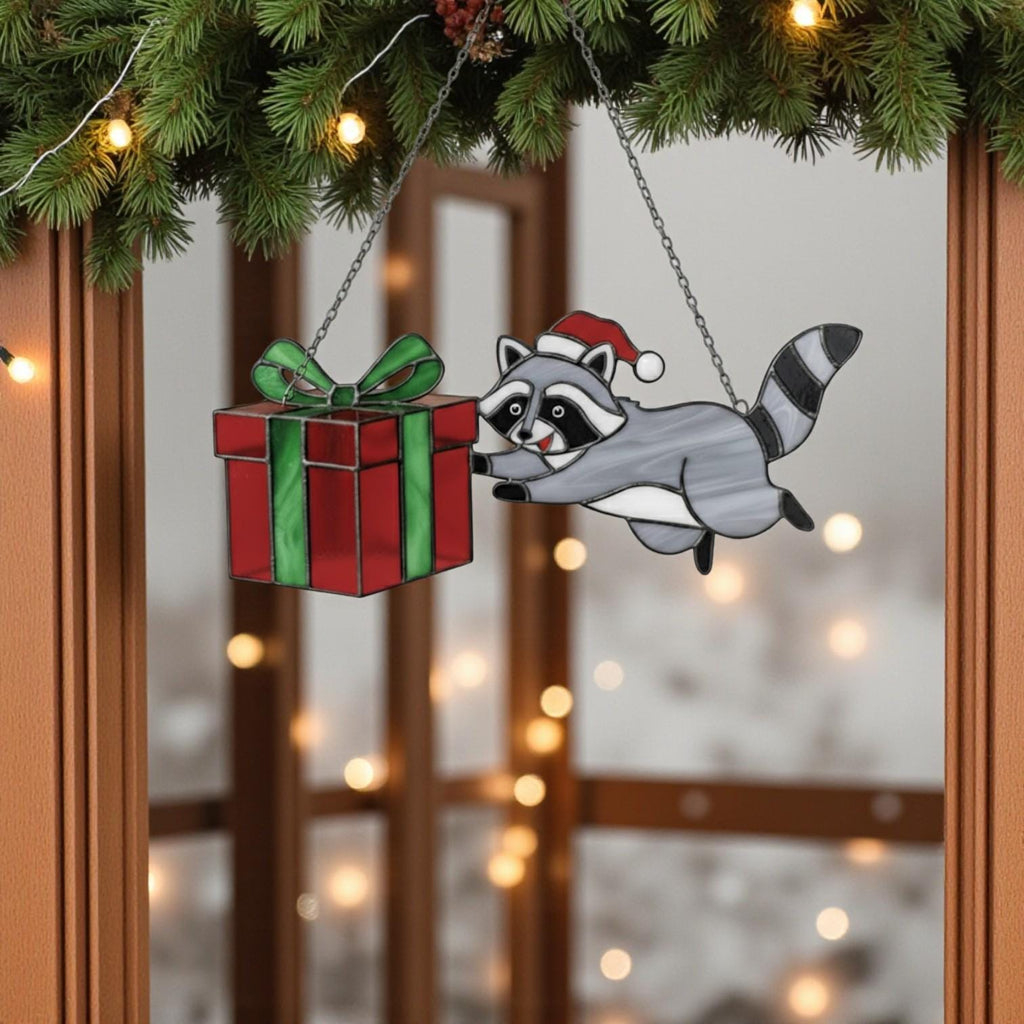 Raccoon stained glass ornament holding red and green gift, Christmas window hanging.