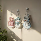 Set of three stained glass snowman ornaments hanging near plants – colorful handmade window decor.