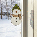 White stained glass snowman on window with forest background – festive winter home decoration.