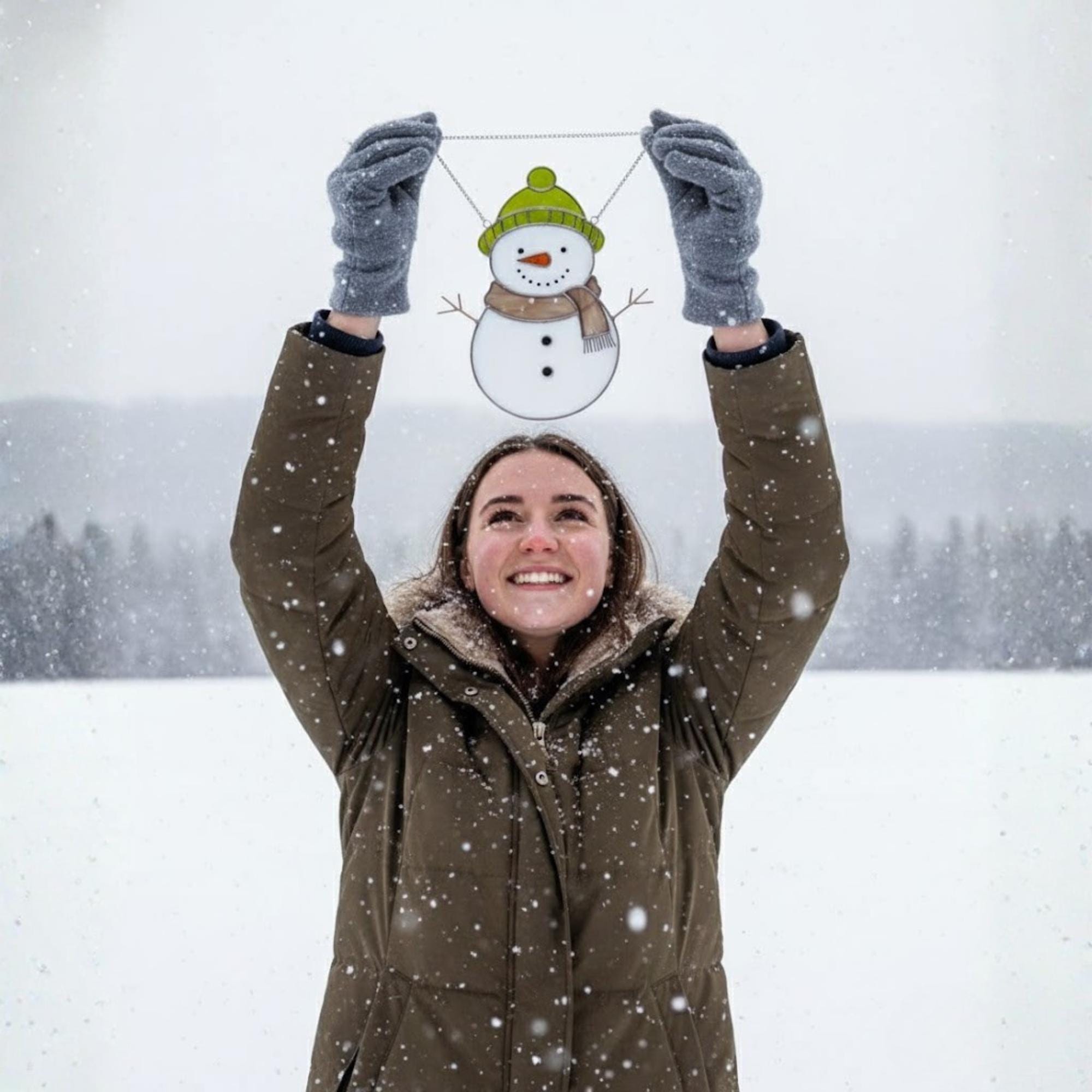 Woman lifting stained glass snowman ornament in snow – holiday winter suncatcher decor idea.