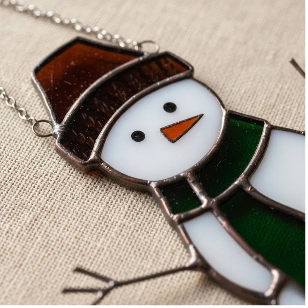 Close-up of snowman ornament with orange scarf – winter handmade glass decor piece.