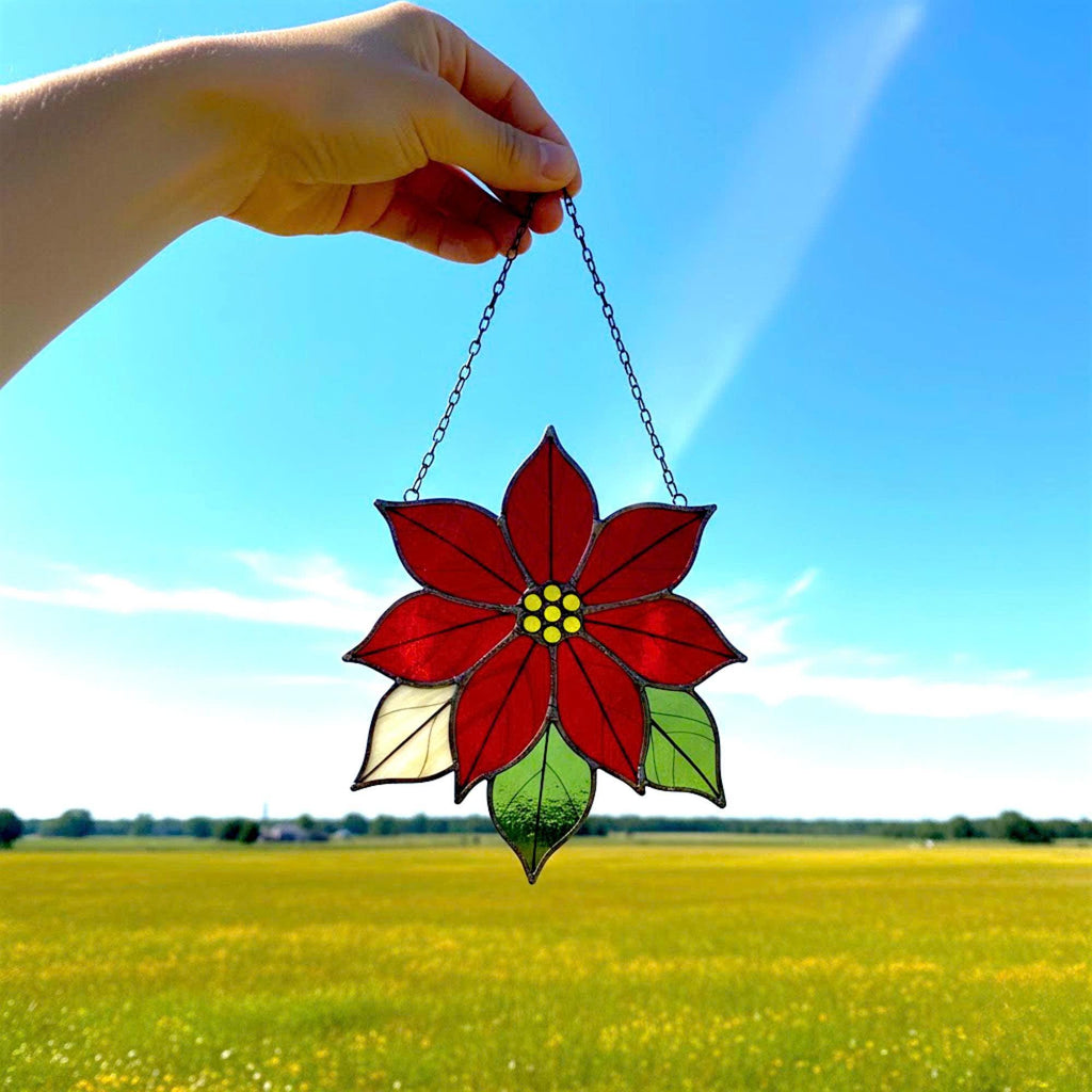 Handmade stained glass poinsettia flower ornament shining in sunlight near window.