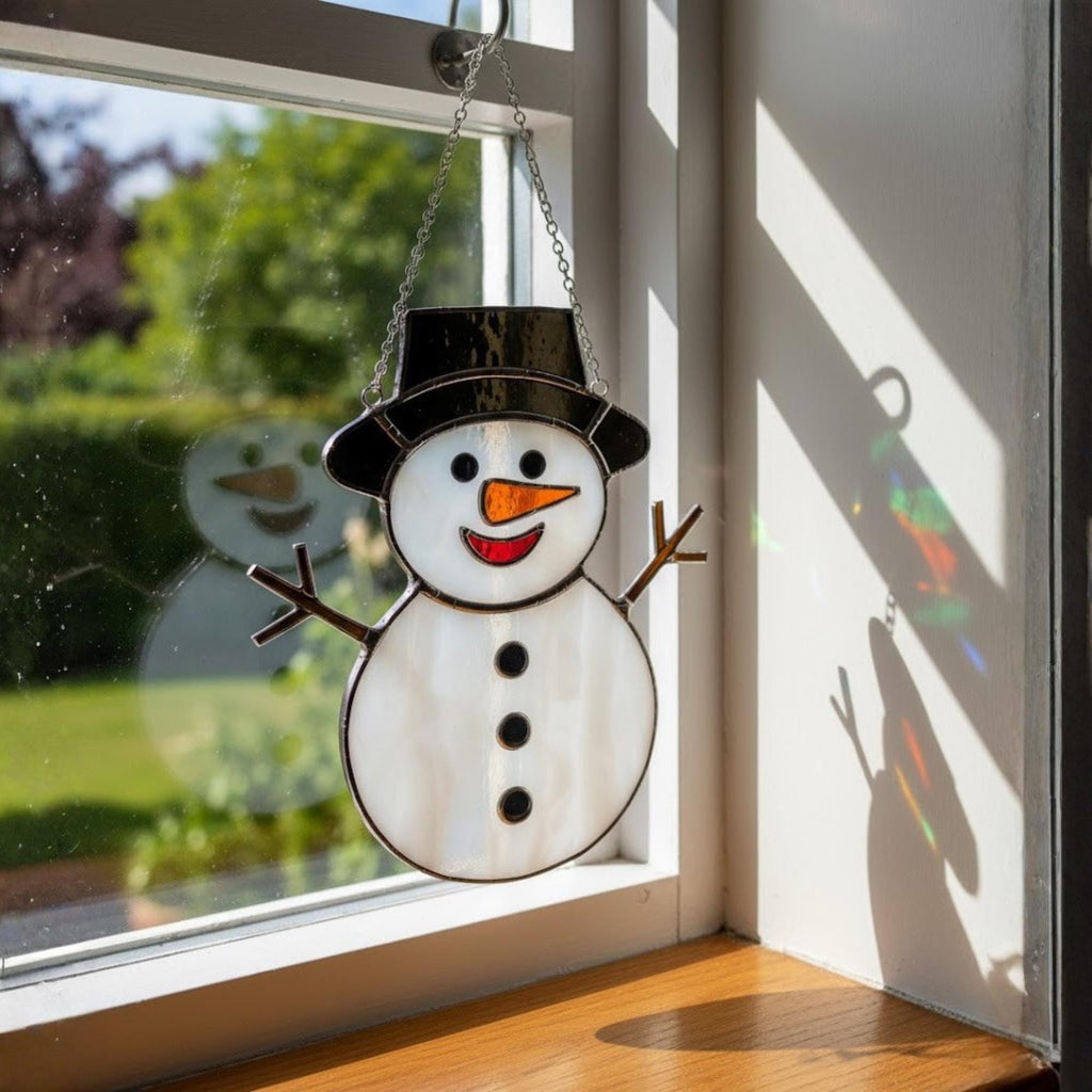 Red hat snowman glass ornament displayed in cozy home window.