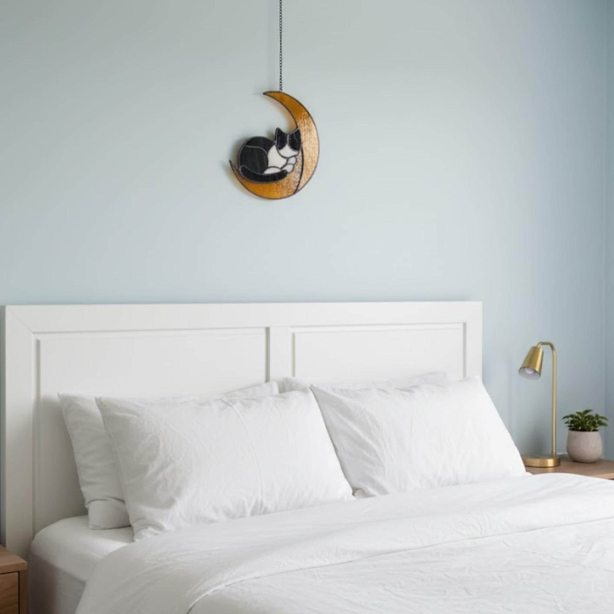 Cat on the moon stained glass window ornament glowing in afternoon sunlight, artistic home accent