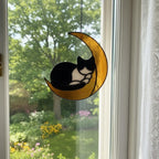 Golden moon stained glass cat ornament in front of white curtains and green garden view
