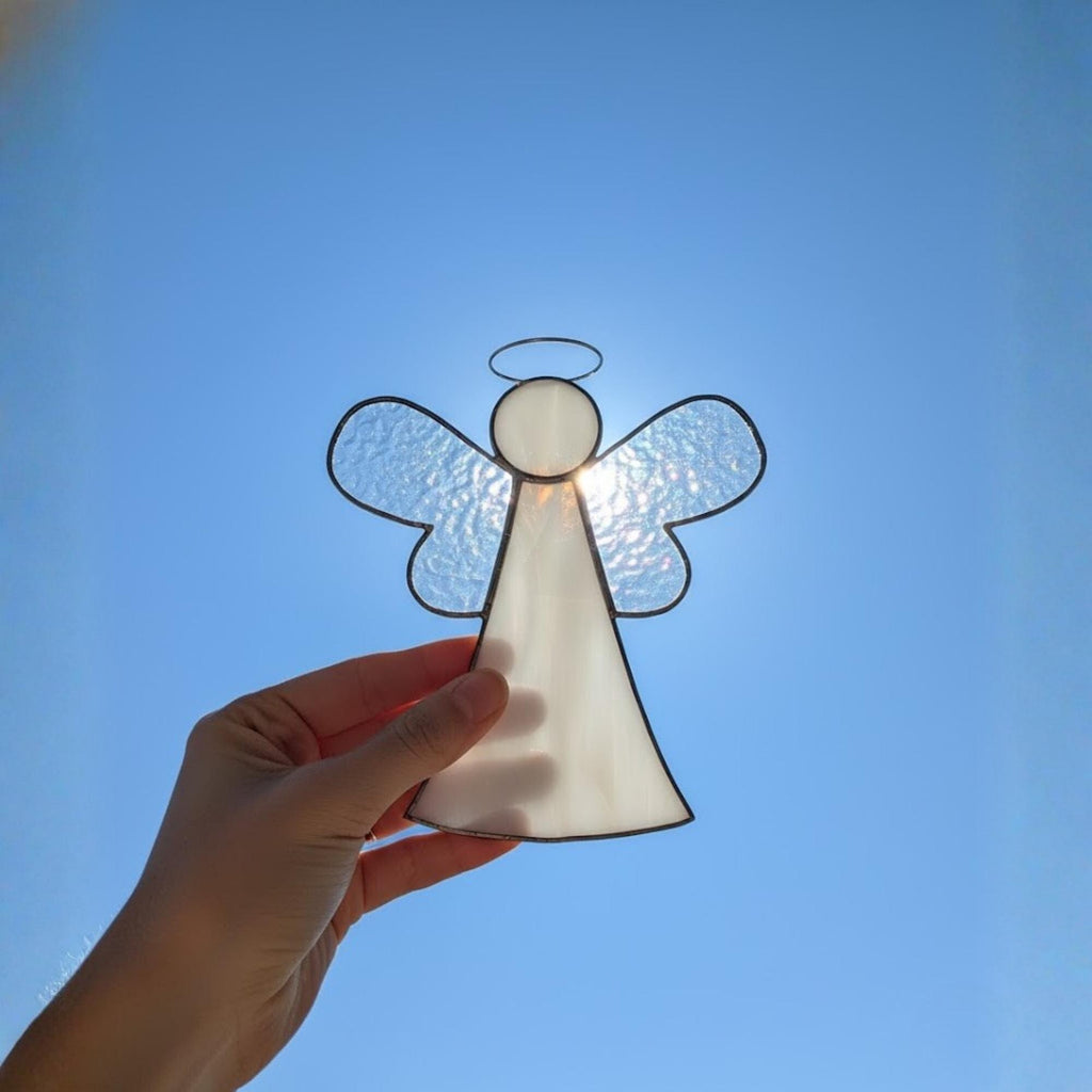Iridescent glass angel ornament shining under sunlight with blue sky background.