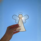 Iridescent glass angel ornament shining under sunlight with blue sky background.