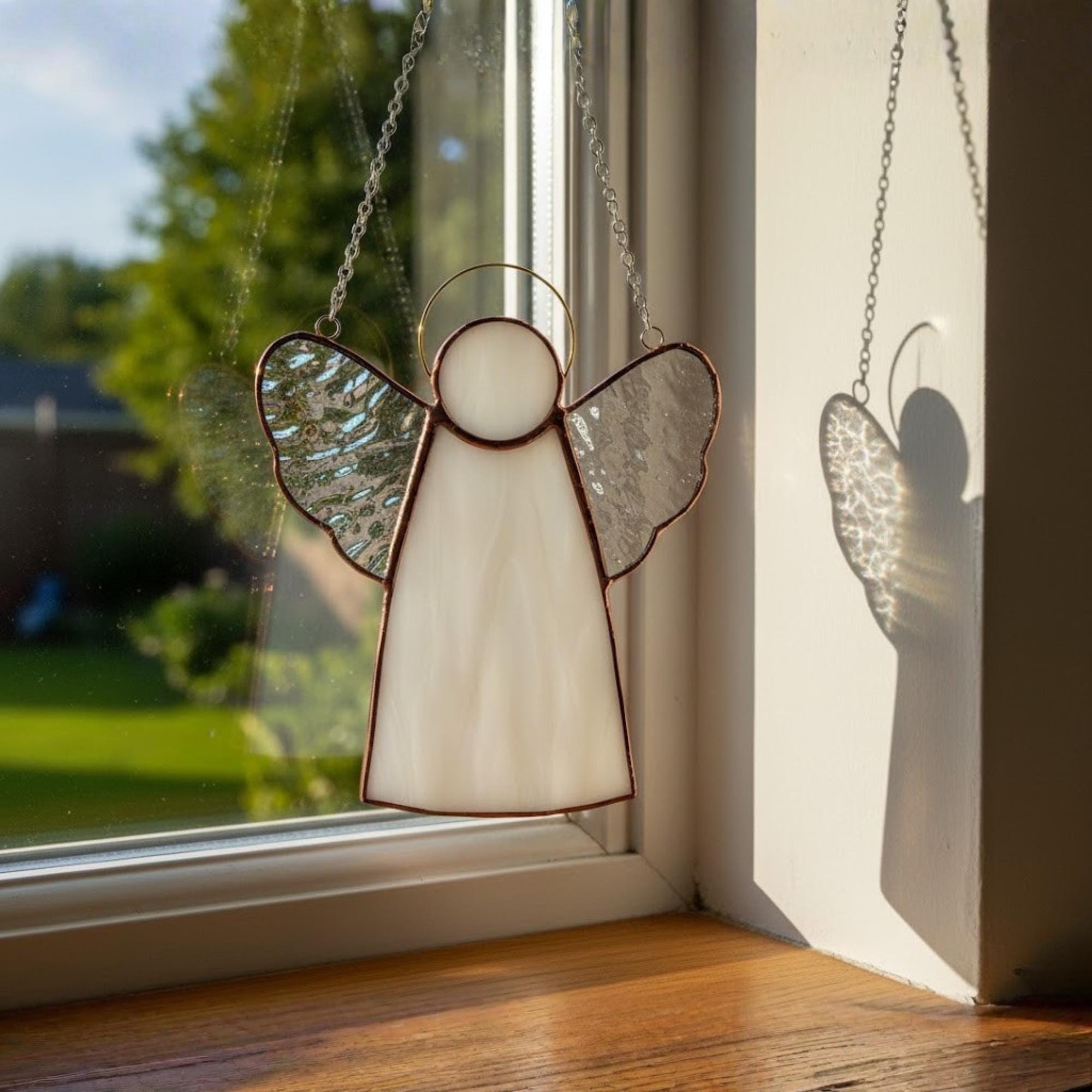 Artistic stained glass angel suncatcher hanging from window hook, reflecting morning light.