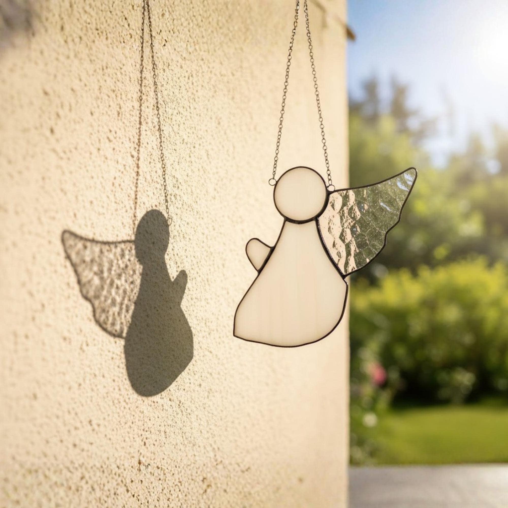 Stained glass angel with textured wings shining beautifully in morning sunlight on windowsill.