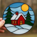 Detailed shot of stained glass winter cottage with golden sun and snow, handmade Christmas suncatcher.