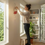 Woman hanging stained glass Christmas cat suncatcher on wall, cozy festive home atmosphere.