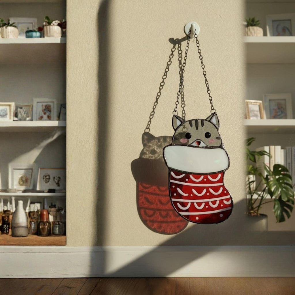 Close-up of Christmas cat stained glass ornament with Santa hat, glowing under warm light.