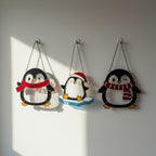 Three penguin glass ornaments hanging on snowy branch, winter scene decor