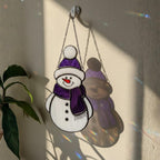 Purple snowman glass ornament hanging indoors – handmade winter window art.
