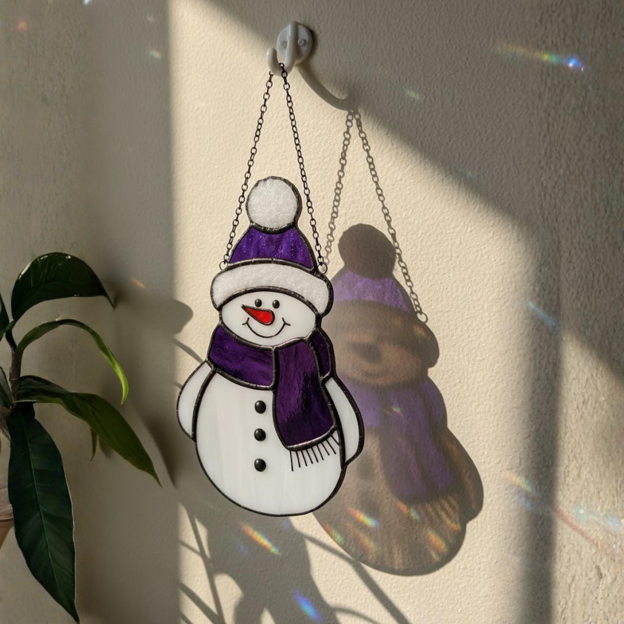Purple snowman glass ornament hanging indoors – handmade winter window art.
