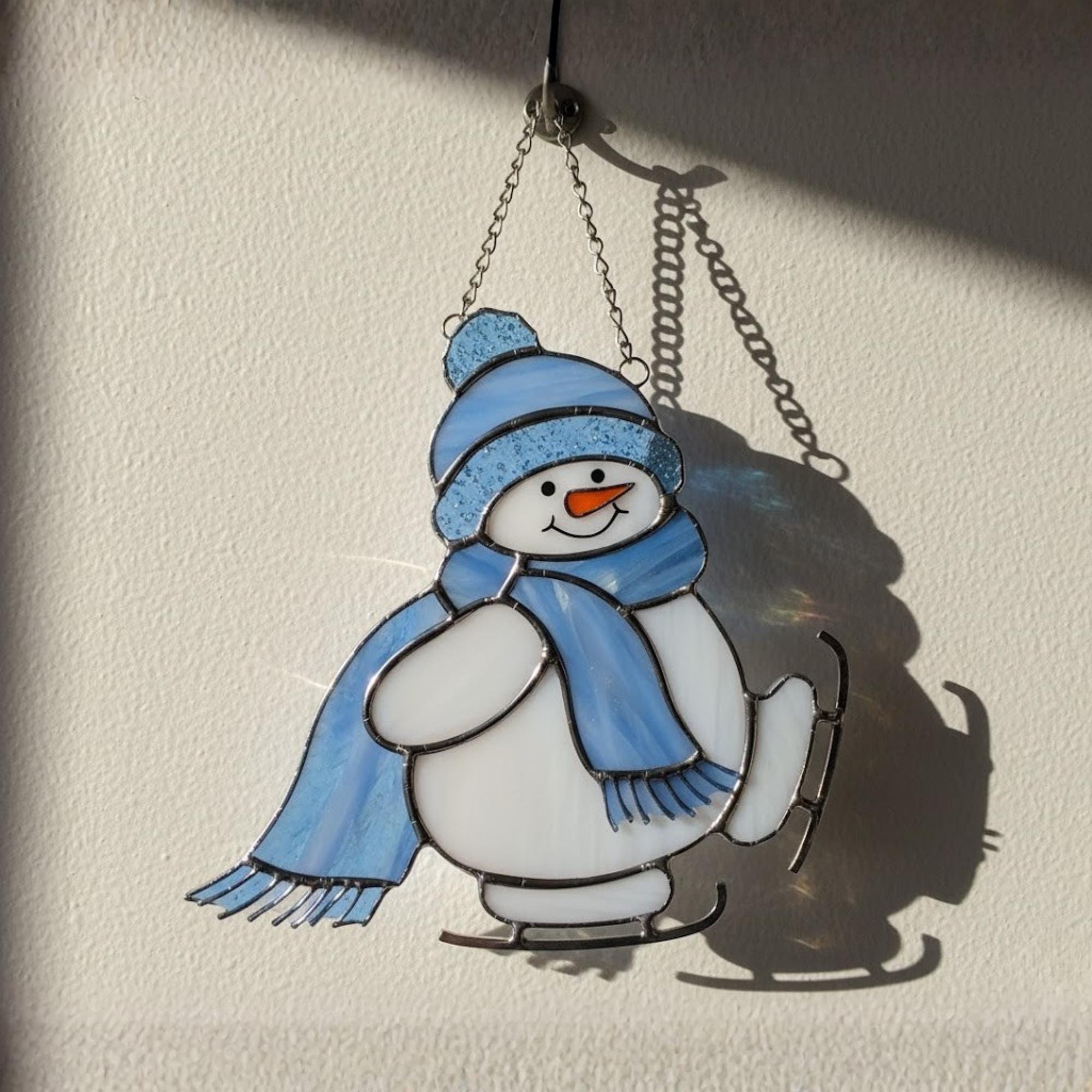 Adorable blue snowman glass ornament catching light – perfect winter home gift.