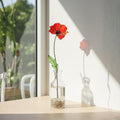 Single stained glass poppy stem on windowsill, sunlight casting shadow