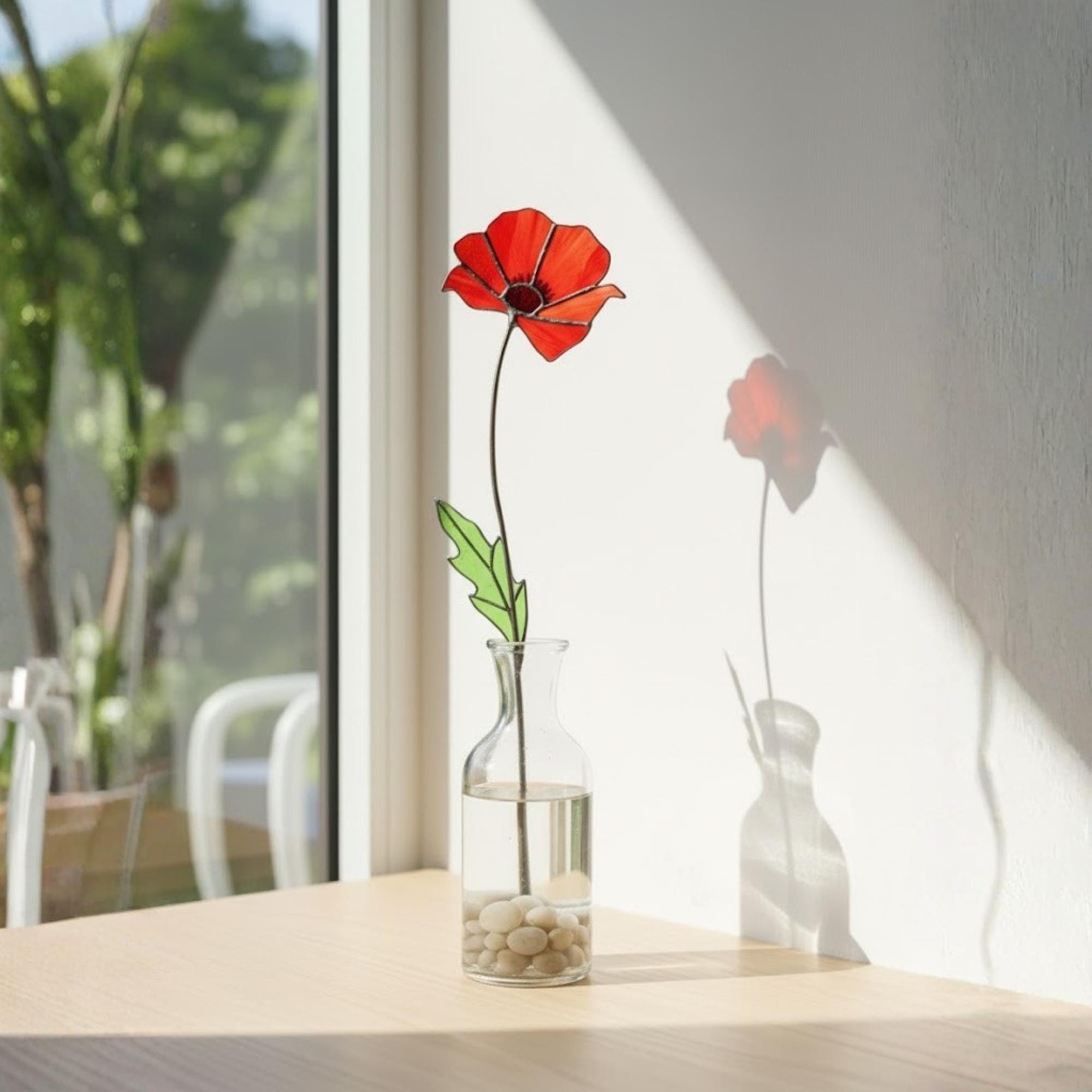 Single stained glass poppy stem on windowsill, sunlight casting shadow