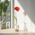 Single stained glass poppy stem on windowsill, sunlight casting shadow