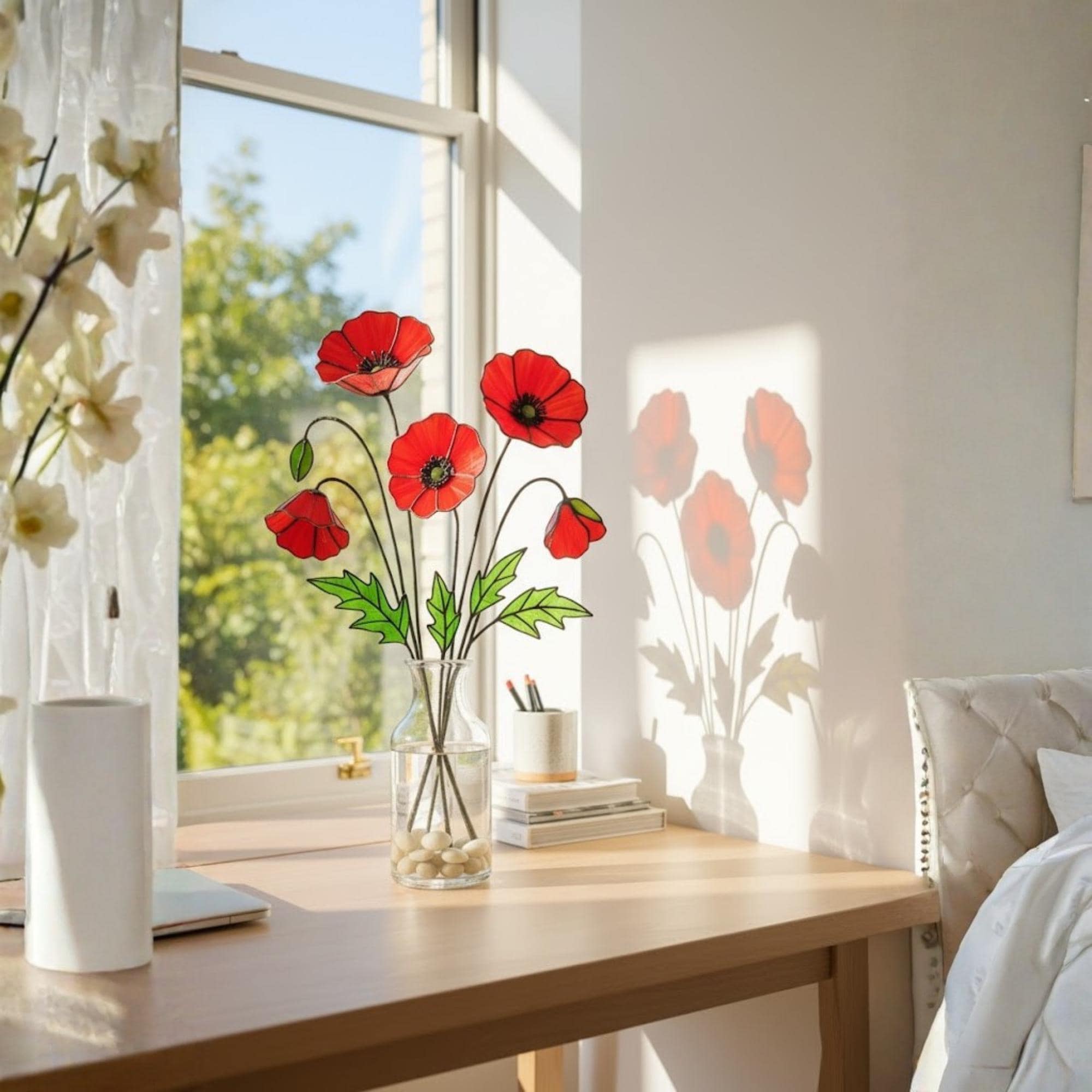 Stained glass poppy flower stems displayed on a windowsill with sunlight reflection