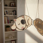 White sleeping dog stained glass ornament glowing in window light.