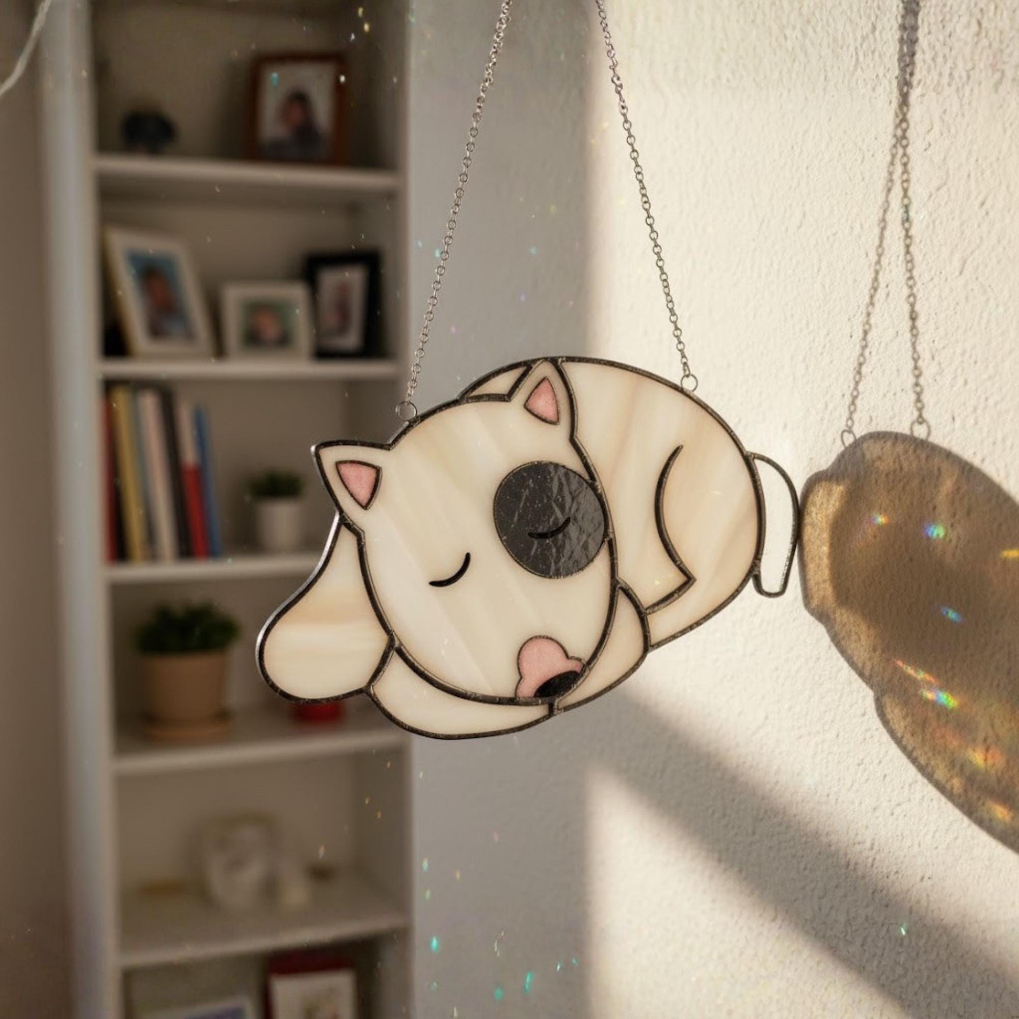 White sleeping dog stained glass ornament glowing in window light.