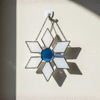 Blue and white stained glass snowflake glowing against sunlight
