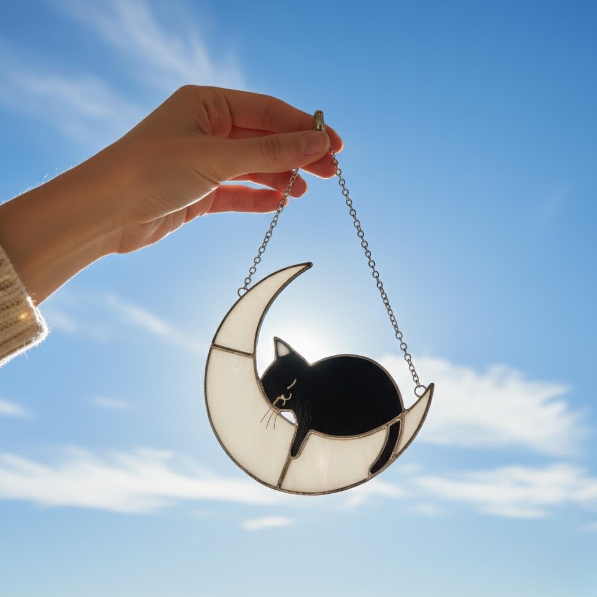 Stained glass cat moon ornament hanging in cozy room, warm window reflections