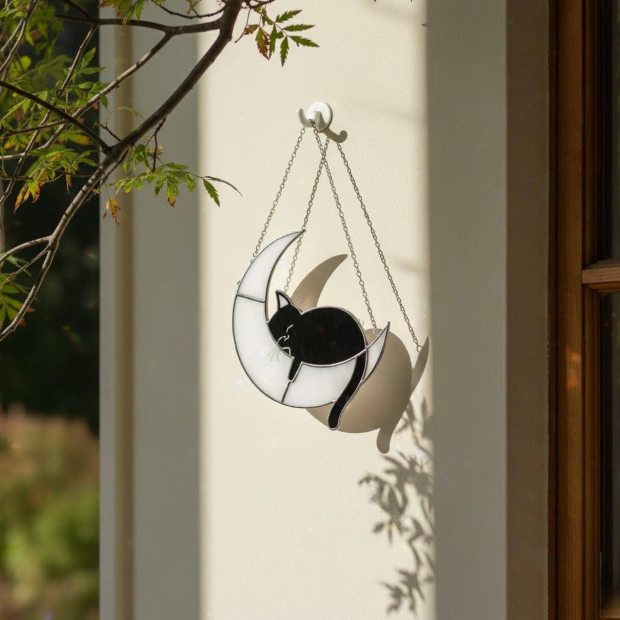 Handmade stained glass cat on the moon suncatcher hanging on tree branch, celestial window decor