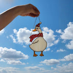 Woman holding goose stained glass ornament under blue sky, whimsical bird decor