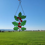 Pair of holly leaf suncatchers displayed outdoors — handmade green glass art.