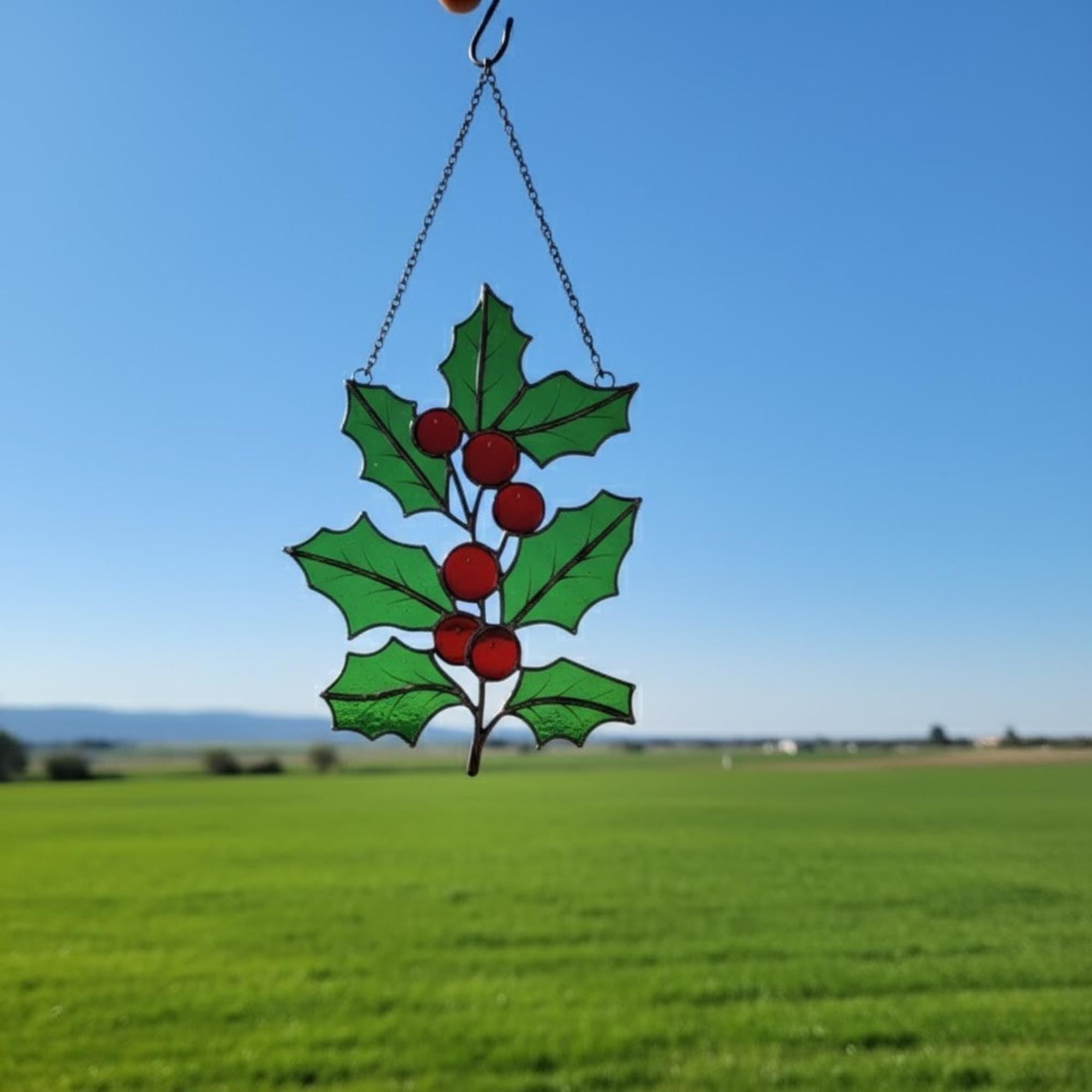 Pair of holly leaf suncatchers displayed outdoors — handmade green glass art.